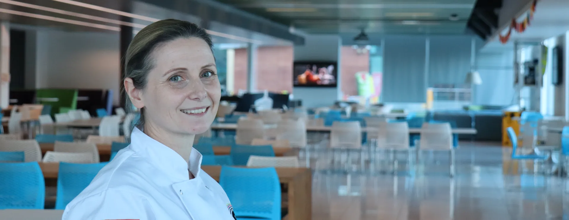 A female chef in the at the front of a dining room. 